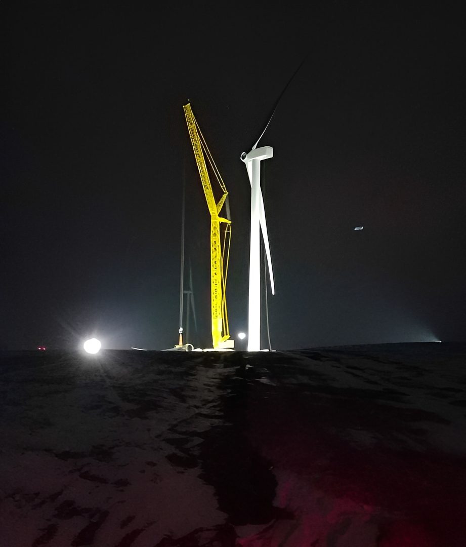 Construction crane beside wind turbine at night.