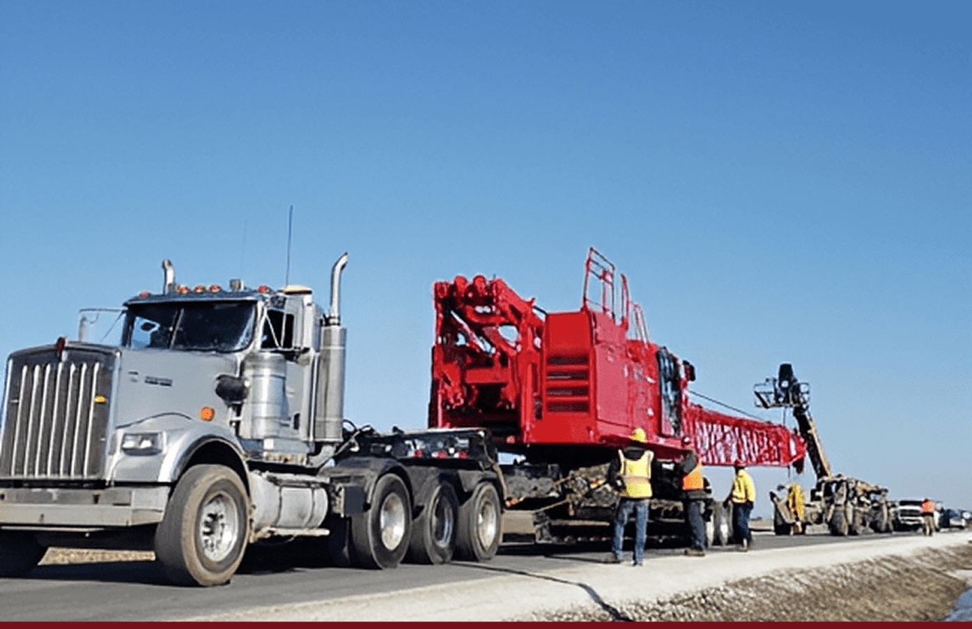 Semi truck hauling red crane boom with workers