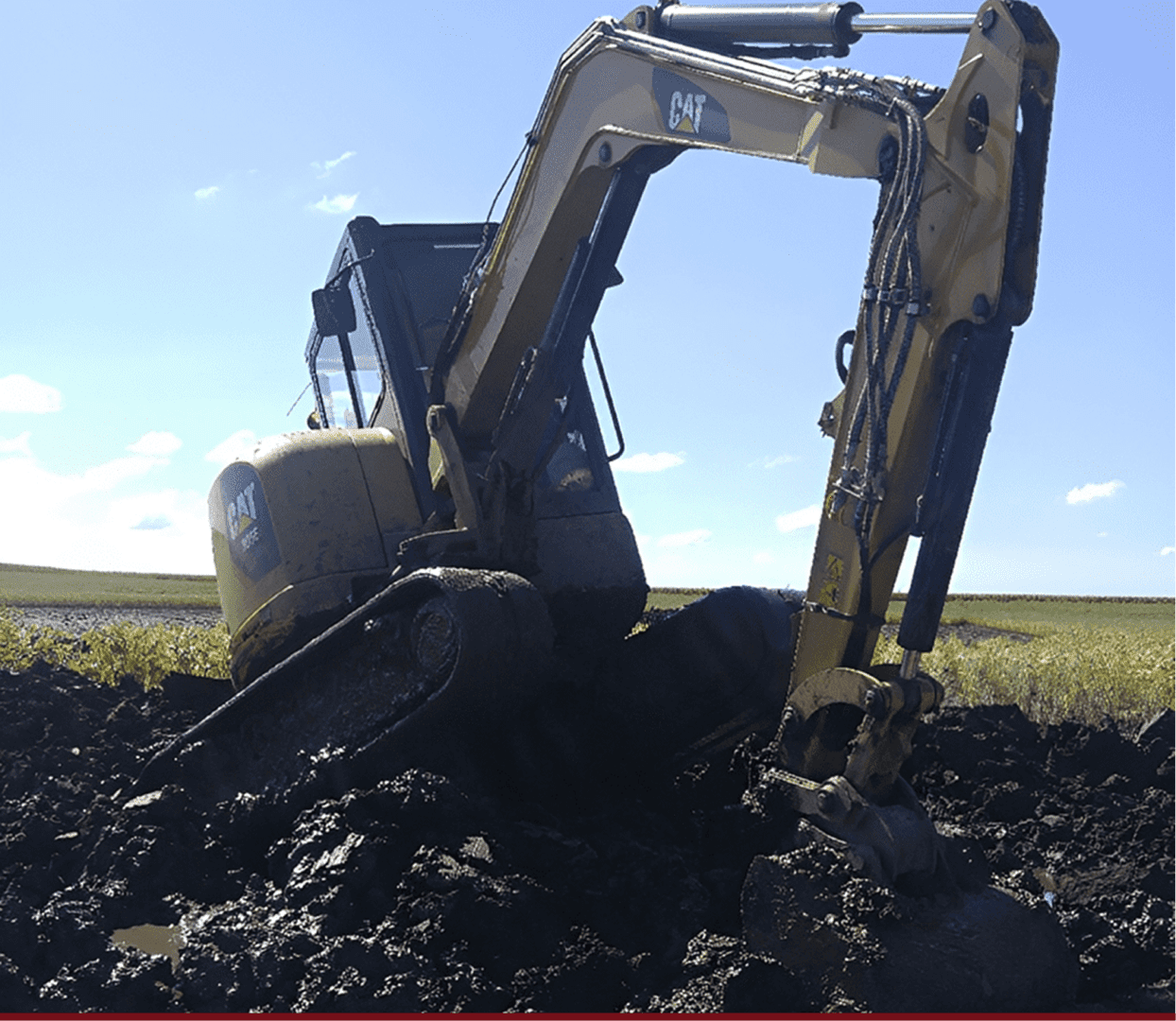 Yellow excavator digging in muddy field