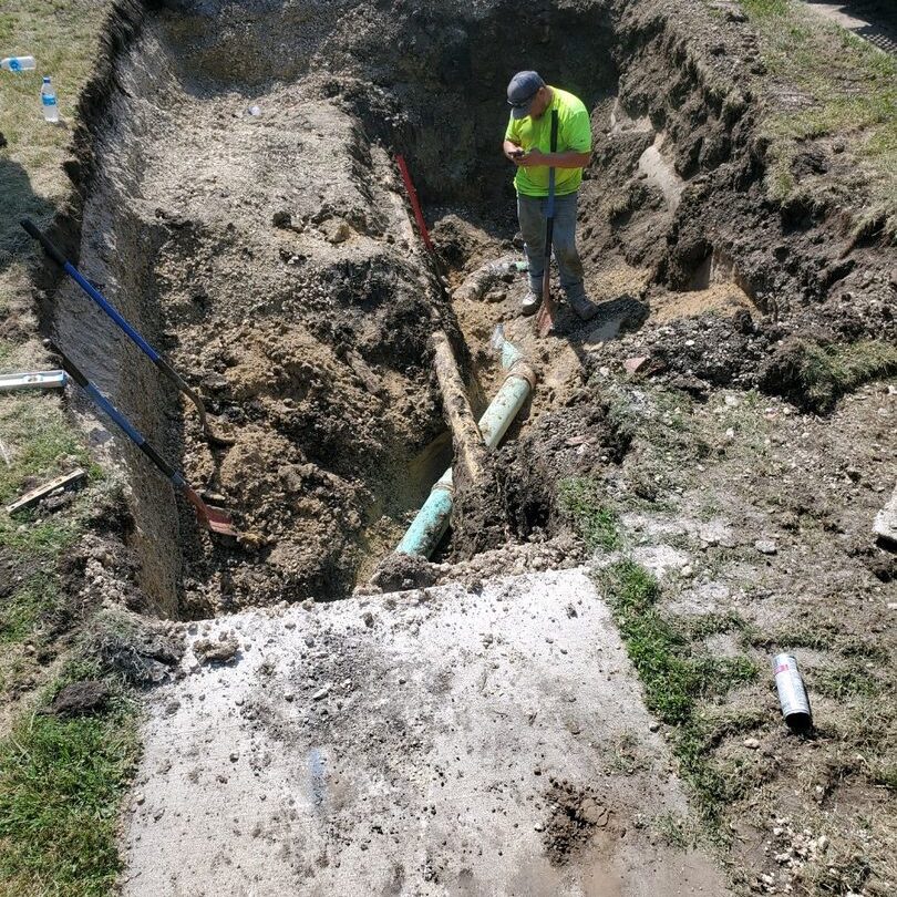 Worker inspecting buried pipe in trench